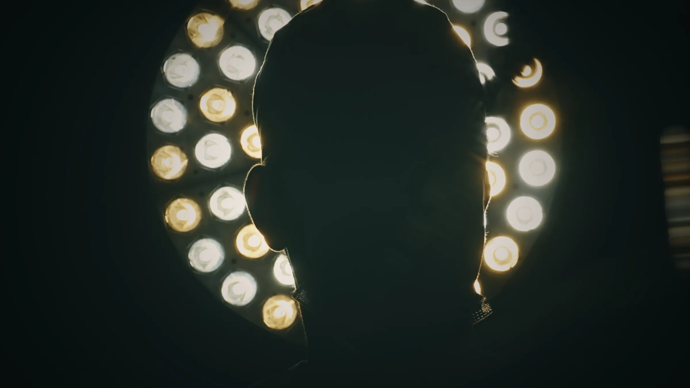 A surgeon in silhouette against the operating lamp. This could be you