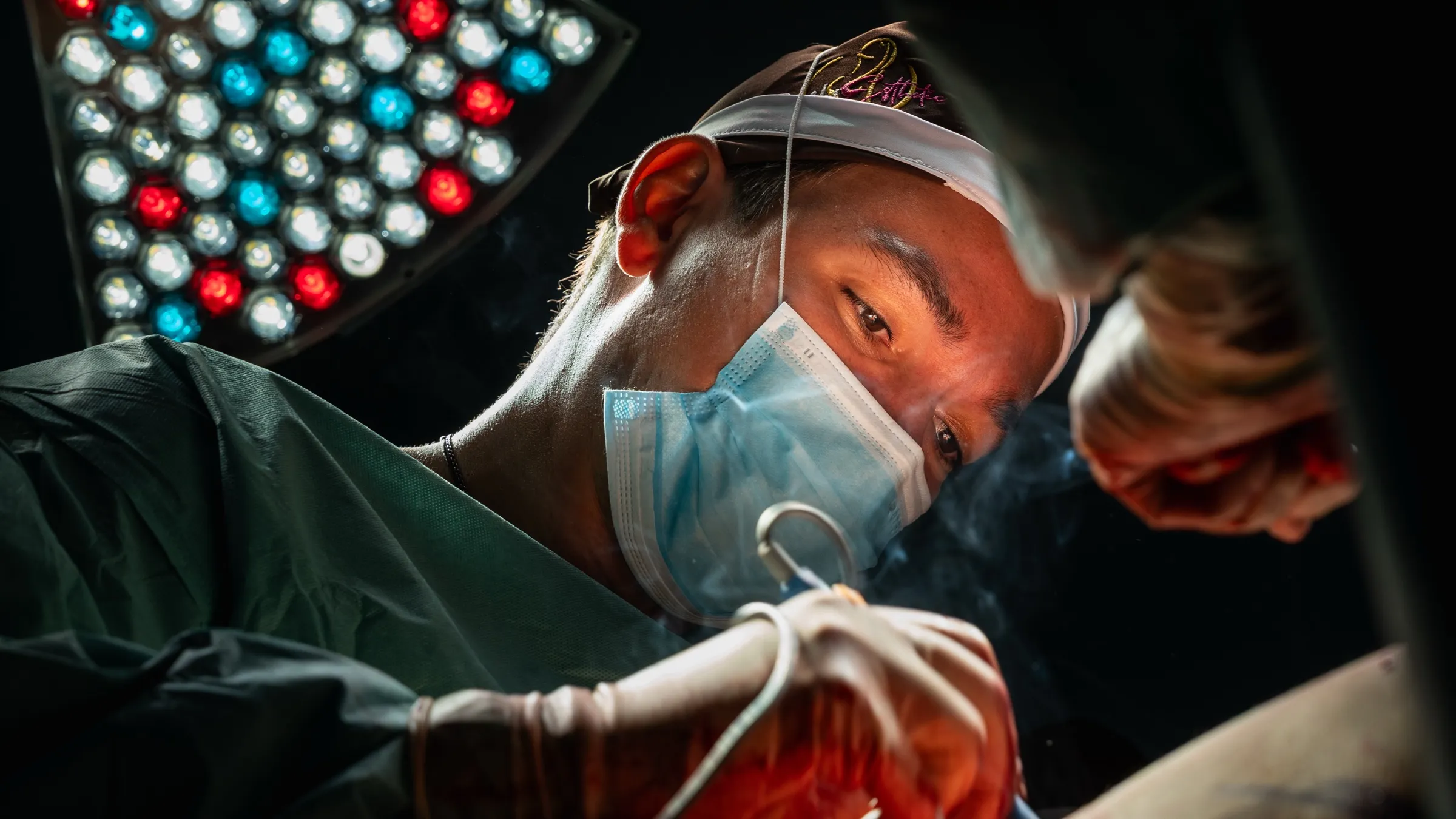 Plastic surgeon operating under red and white surgical lights